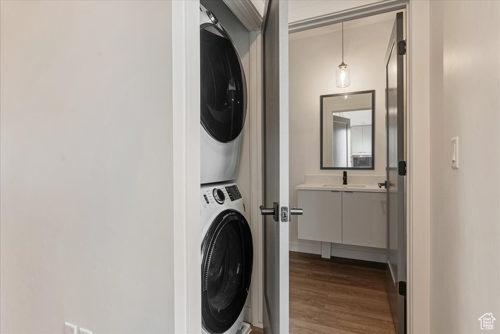 Laundry room with stacked washer and dryer, dark hardwood / wood-style flooring, and sink