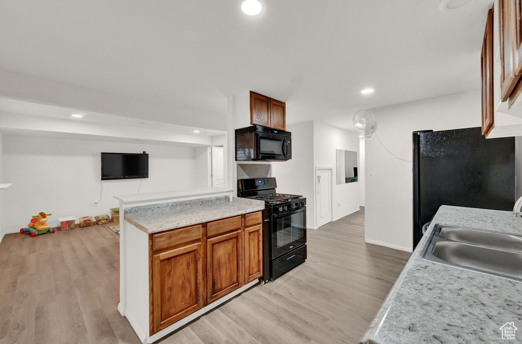 Kitchen featuring light wood-type flooring, black appliances, light stone counters, and sink