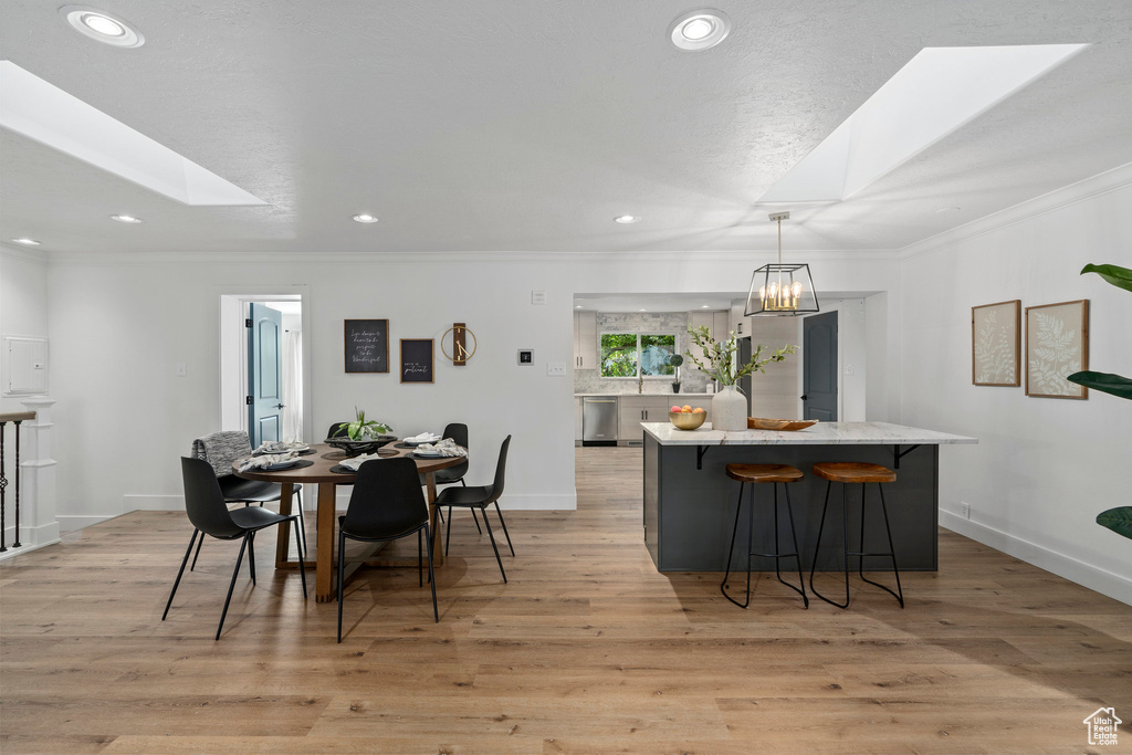Dining space with light hardwood / wood-style floors, a skylight, and a notable chandelier