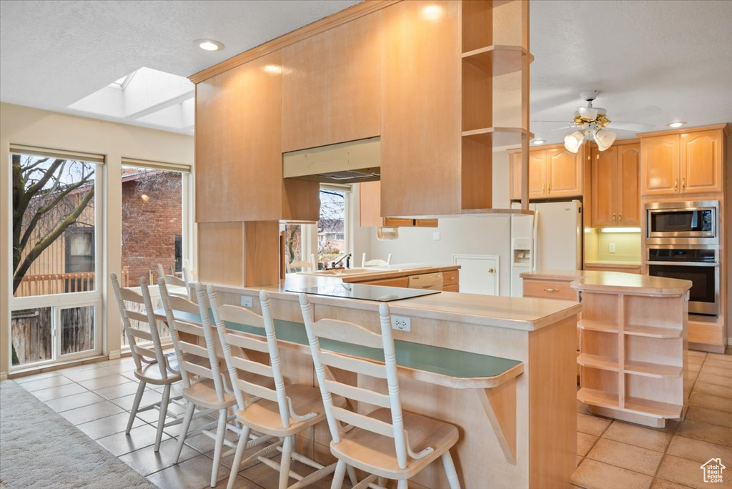 Kitchen with a kitchen bar, ceiling fan, light tile floors, and stainless steel appliances
