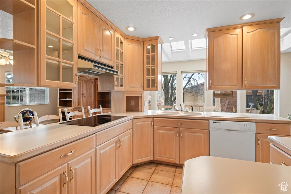 Kitchen with light brown cabinets, black electric cooktop, dishwasher, sink, and light tile floors