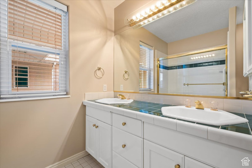 Bathroom with dual sinks, large vanity, tile floors, and backsplash