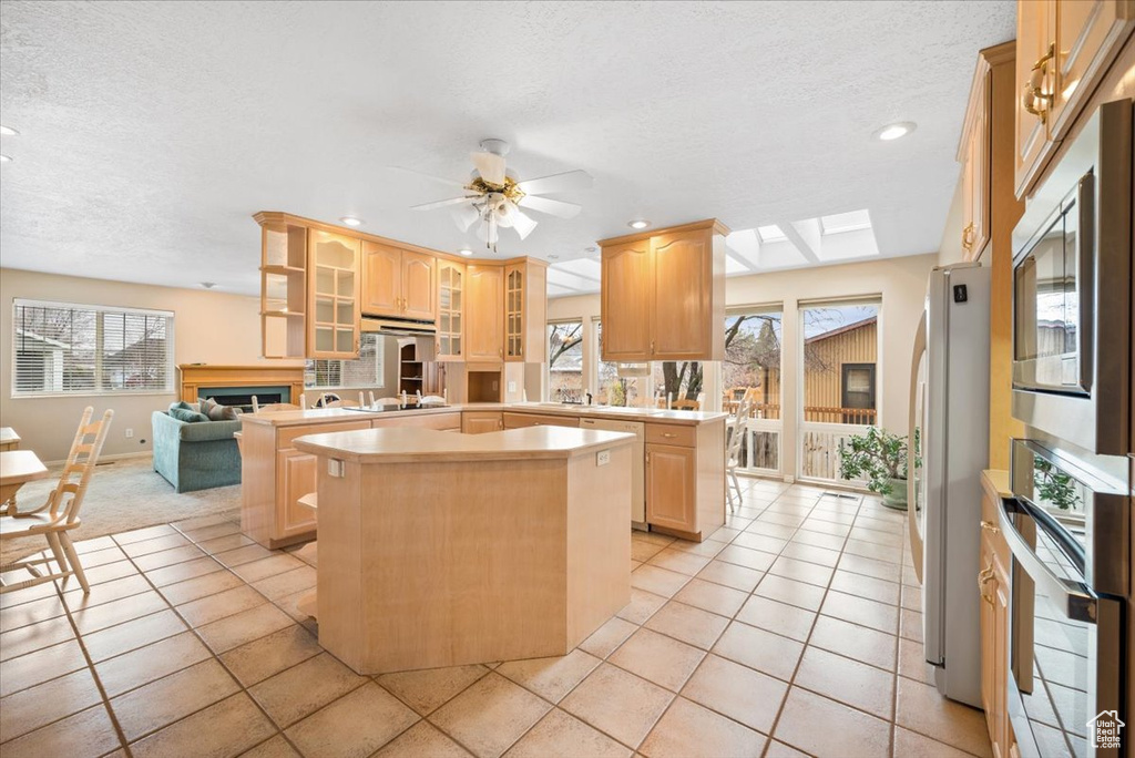 Kitchen with stainless steel appliances, a skylight, an island with sink, light tile floors, and ceiling fan