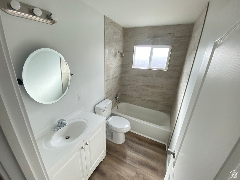 Full bathroom with hardwood / wood-style flooring, vanity, tiled shower / bath combo, and toilet