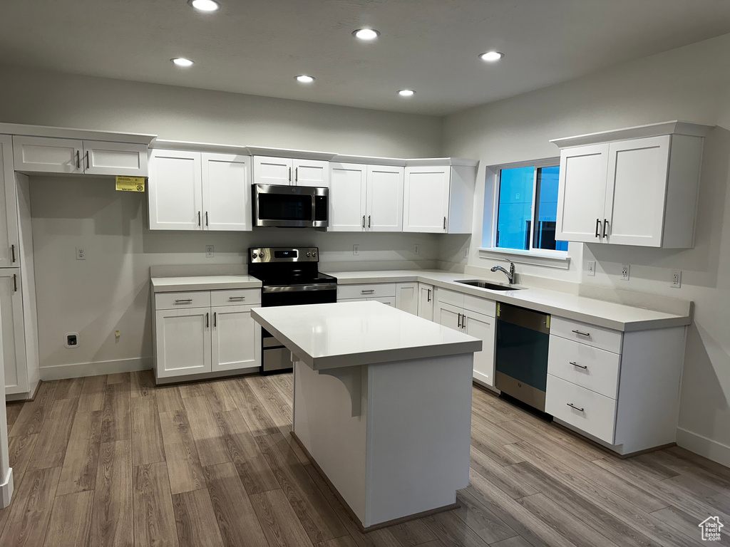 Kitchen featuring light hardwood / wood-style floors, white cabinets, a center island, sink, and appliances with stainless steel finishes