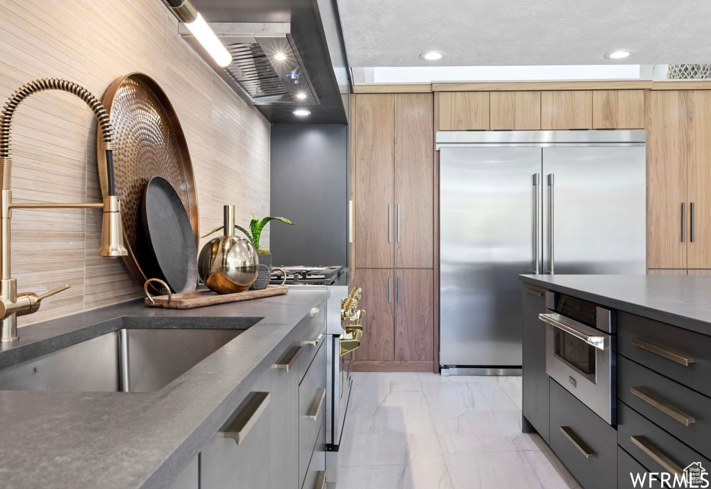 Kitchen featuring tasteful backsplash, premium appliances, sink, and light tile floors
