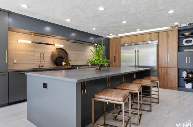 Kitchen featuring a kitchen island, a textured ceiling, a breakfast bar area, sink, and stainless steel built in fridge