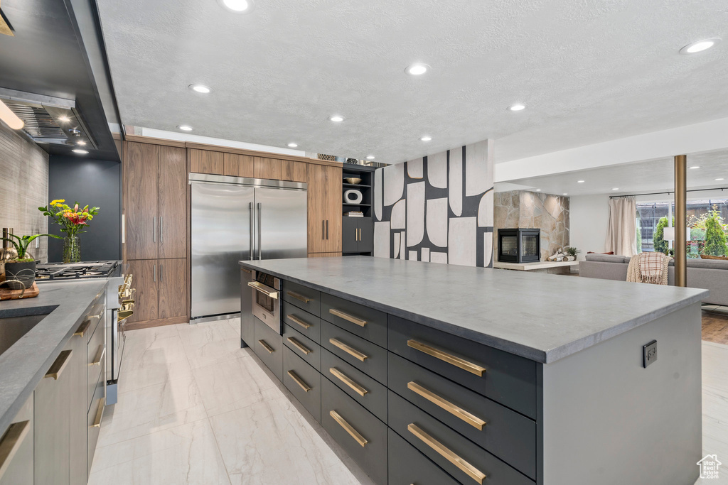 Kitchen with built in fridge, a fireplace, a center island, light tile flooring, and gray cabinetry