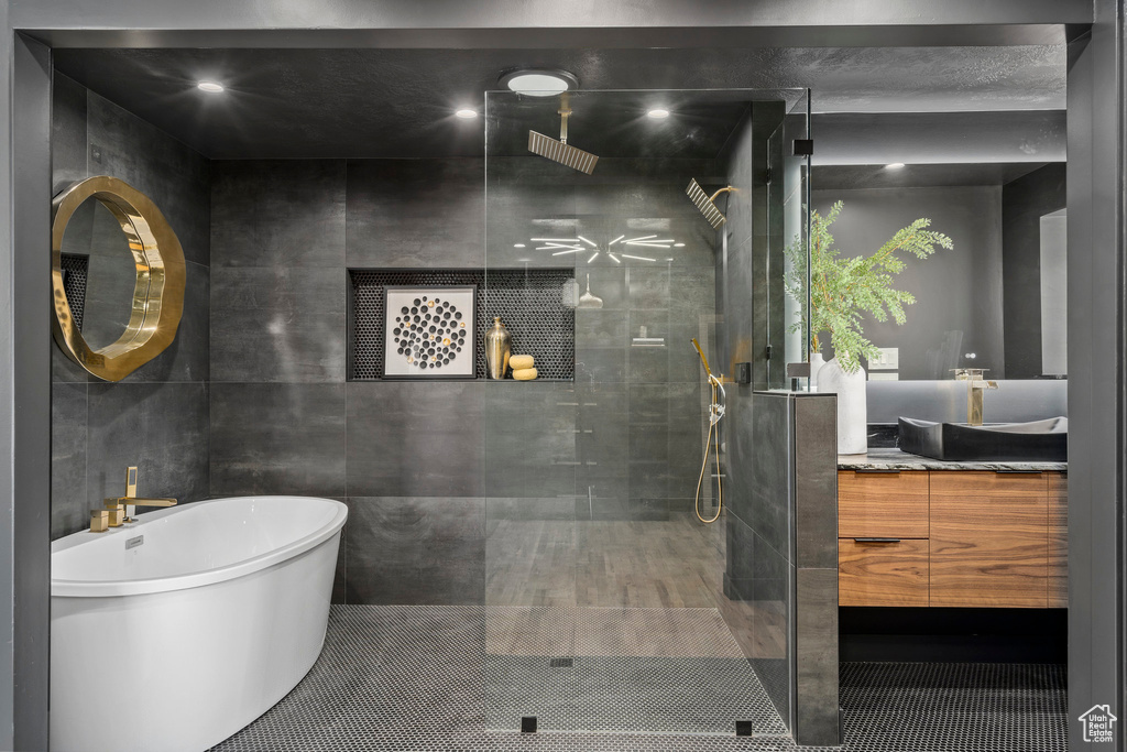Bathroom featuring tile walls, shower with separate bathtub, and vanity with extensive cabinet space