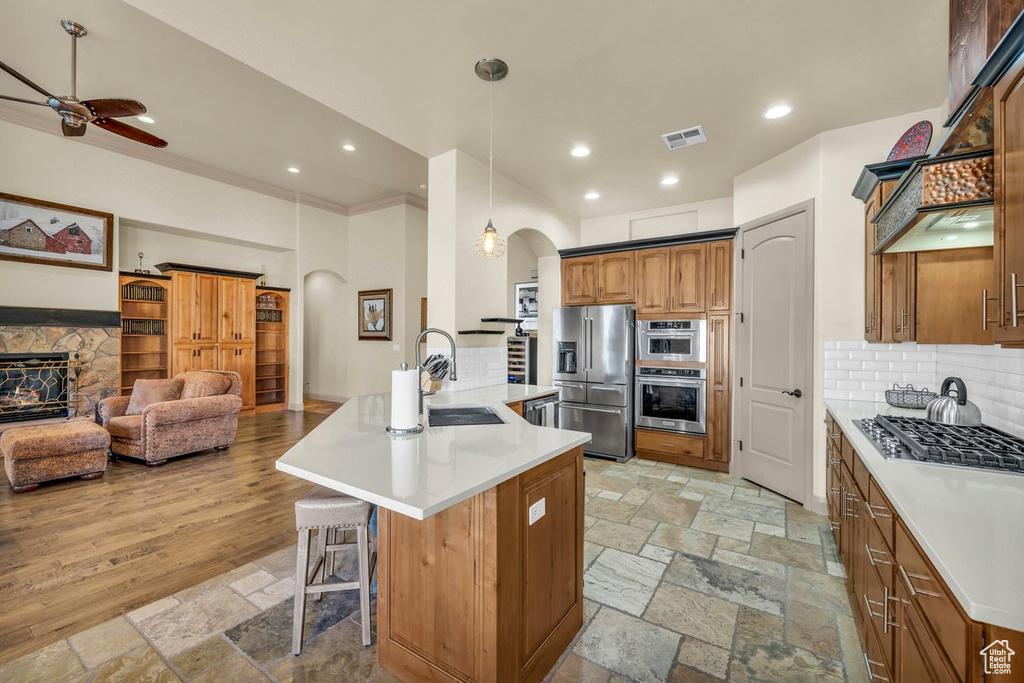 Kitchen with light wood-type flooring, tasteful backsplash, an island with sink, decorative light fixtures, and ceiling fan