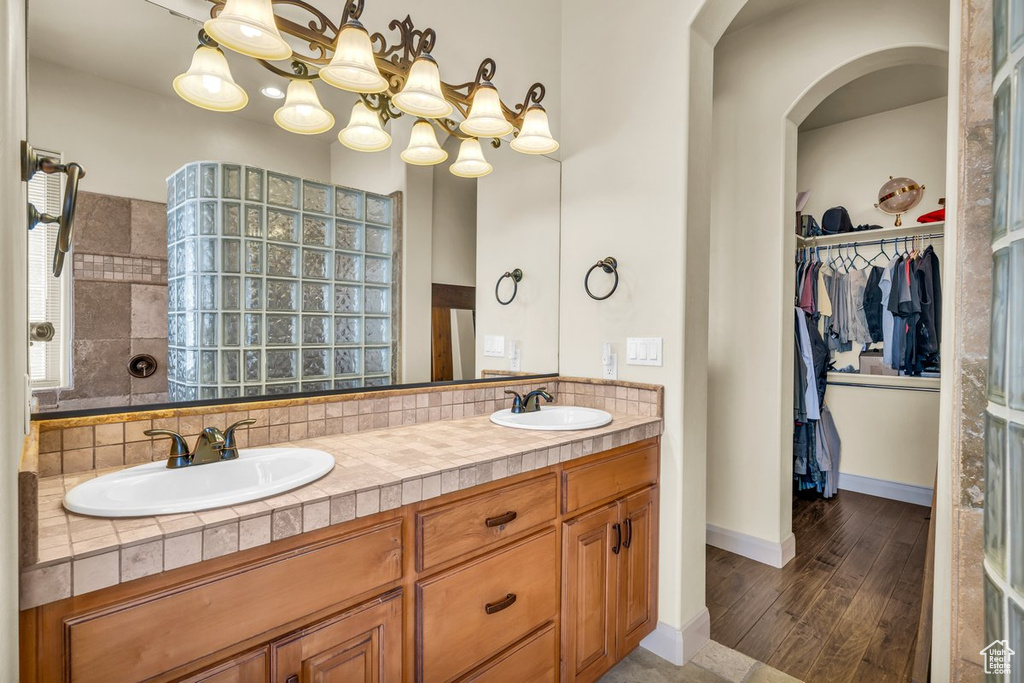 Bathroom with hardwood / wood-style floors, a notable chandelier, tiled shower, vanity with extensive cabinet space, and dual sinks