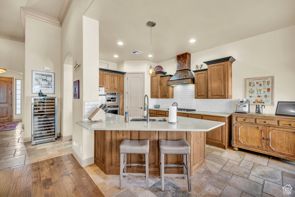 Kitchen with backsplash, light wood-type flooring, custom range hood, beverage cooler, and sink