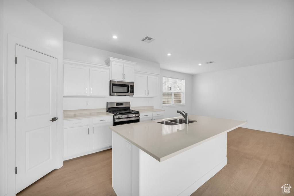 Kitchen with white cabinets, appliances with stainless steel finishes, light hardwood / wood-style flooring, an island with sink, and sink