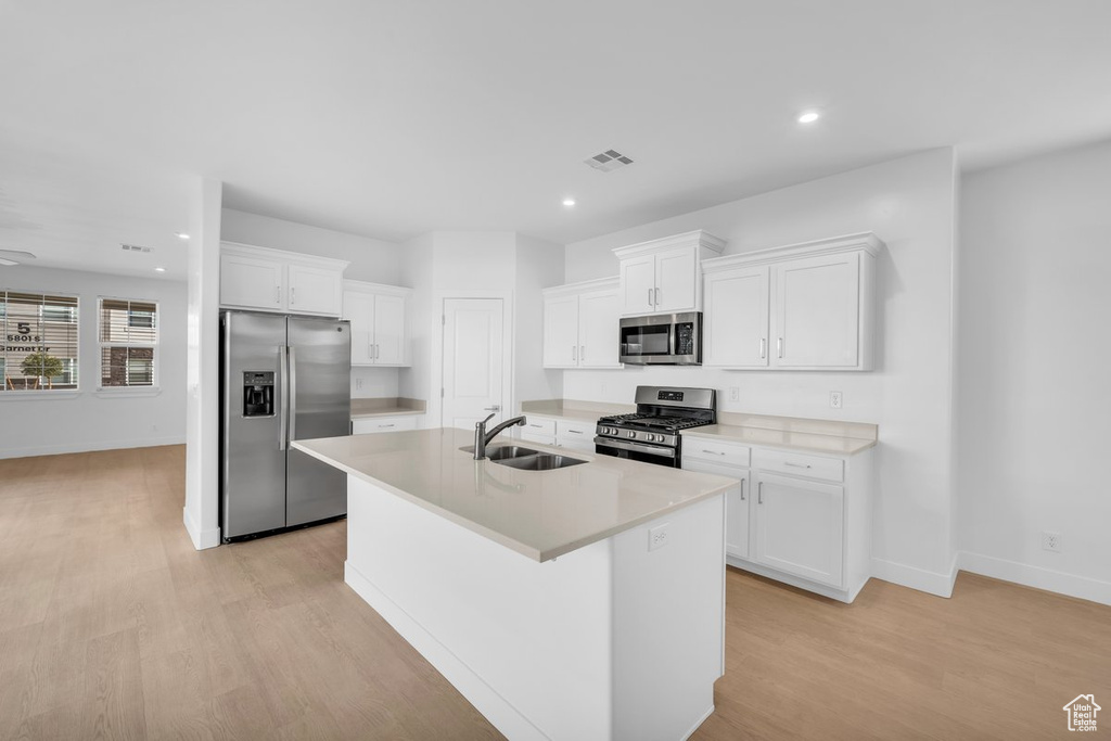 Kitchen featuring light wood-type flooring, white cabinets, appliances with stainless steel finishes, an island with sink, and sink