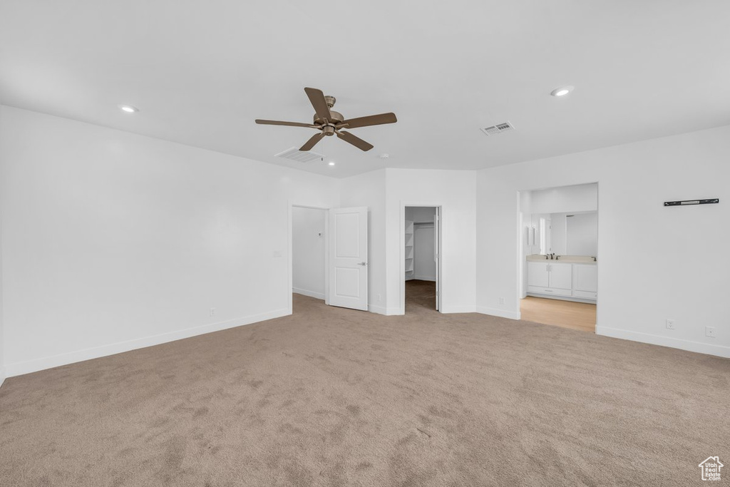 Unfurnished bedroom with connected bathroom, a spacious closet, ceiling fan, and light carpet