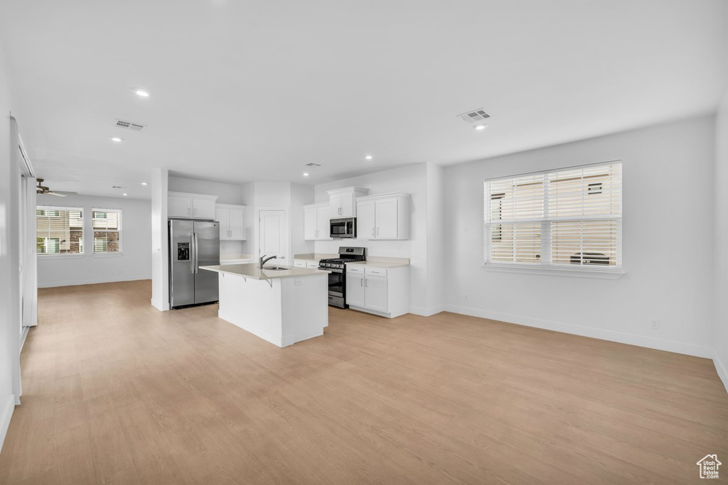 Kitchen featuring white cabinets, light hardwood / wood-style flooring, stainless steel appliances, and a center island with sink