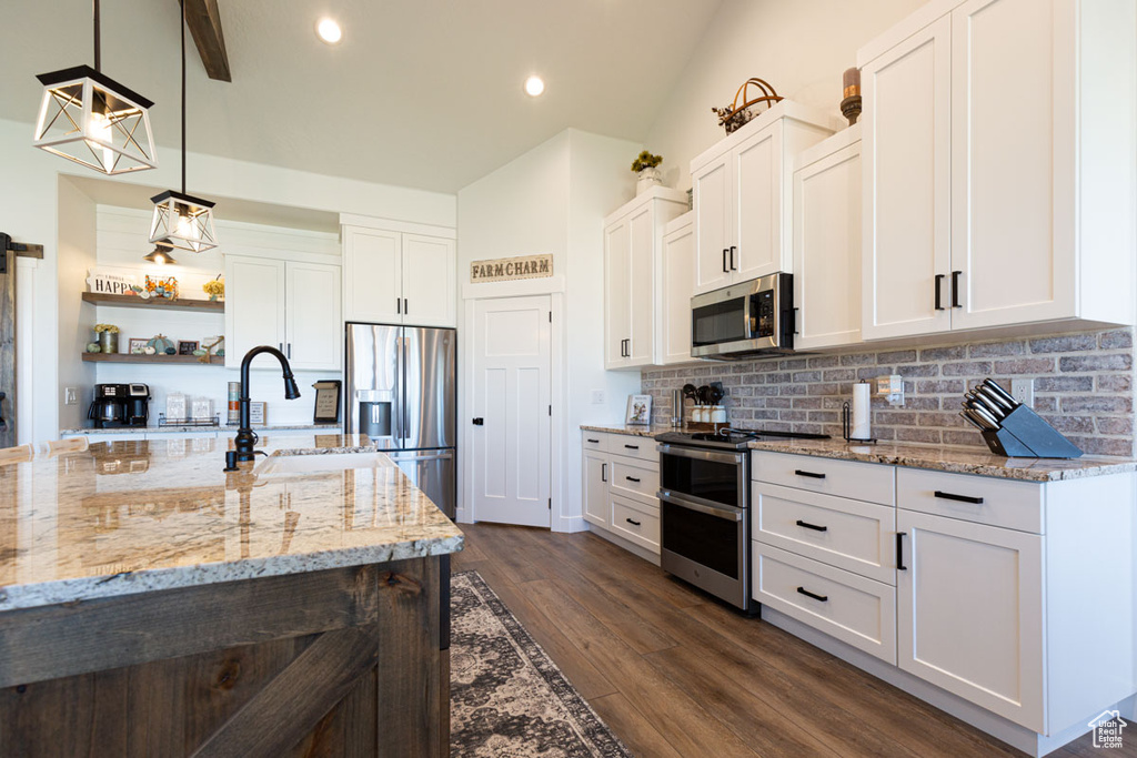 Kitchen featuring white cabinets, dark wood-type flooring, vaulted ceiling, decorative light fixtures, and appliances with stainless steel finishes