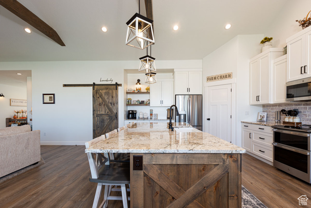 Kitchen with white cabinetry, a barn door, appliances with stainless steel finishes, and a center island with sink
