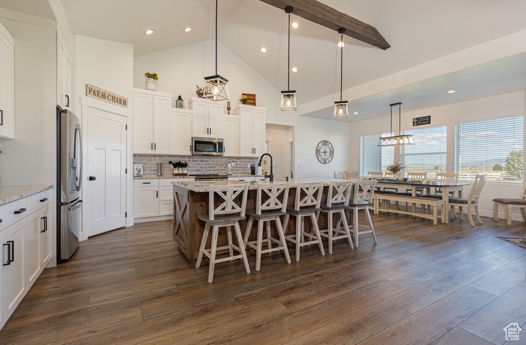 Kitchen featuring white cabinets, hanging light fixtures, dark wood-type flooring, and a center island with sink