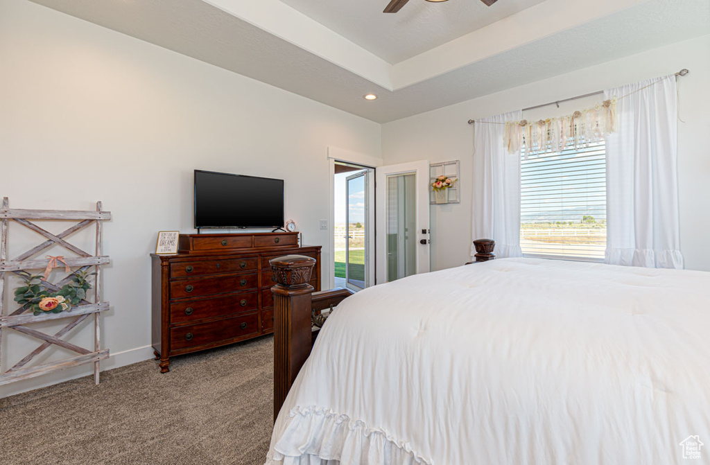 Carpeted bedroom with ceiling fan, a raised ceiling, and access to exterior