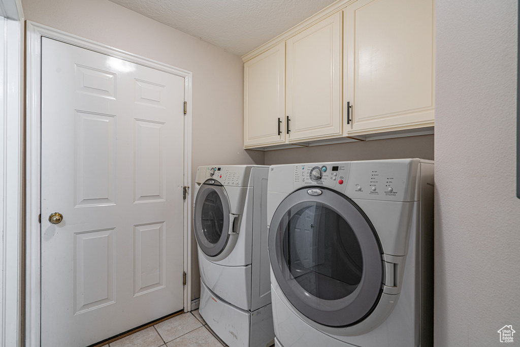 Washroom featuring light tile flooring, washer and clothes dryer, and cabinets