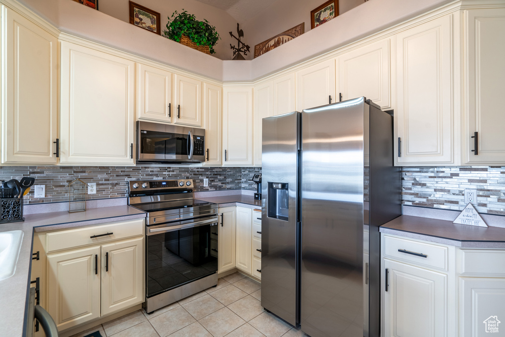 Kitchen featuring light tile flooring, stainless steel appliances, backsplash, and white cabinetry