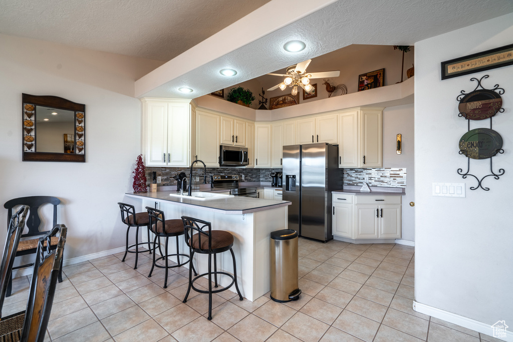 Kitchen featuring stainless steel appliances, white cabinets, tasteful backsplash, light tile floors, and ceiling fan