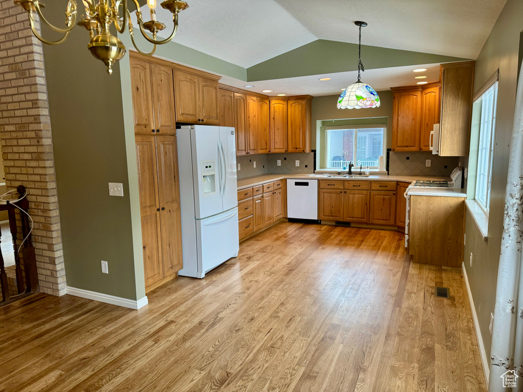 Kitchen featuring white appliances, decorative light fixtures, light wood-type flooring, and tasteful backsplash