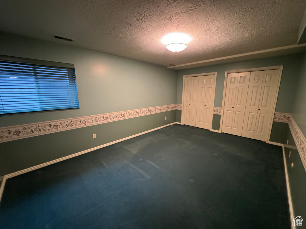 Unfurnished bedroom featuring dark colored carpet, multiple closets, and a textured ceiling