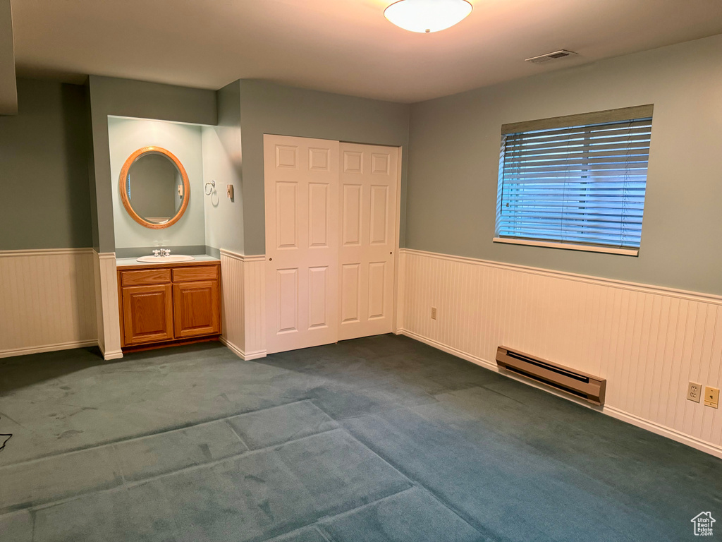 Unfurnished bedroom with baseboard heating, a closet, dark colored carpet, sink, and connected bathroom