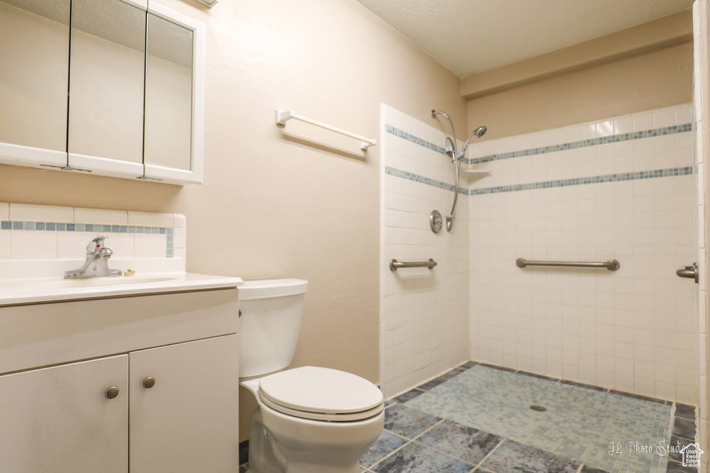Bathroom with tile floors, oversized vanity, a tile shower, and toilet