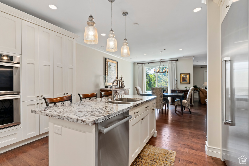 Kitchen featuring hanging light fixtures, stainless steel appliances, an island with sink, sink, and dark wood-type flooring