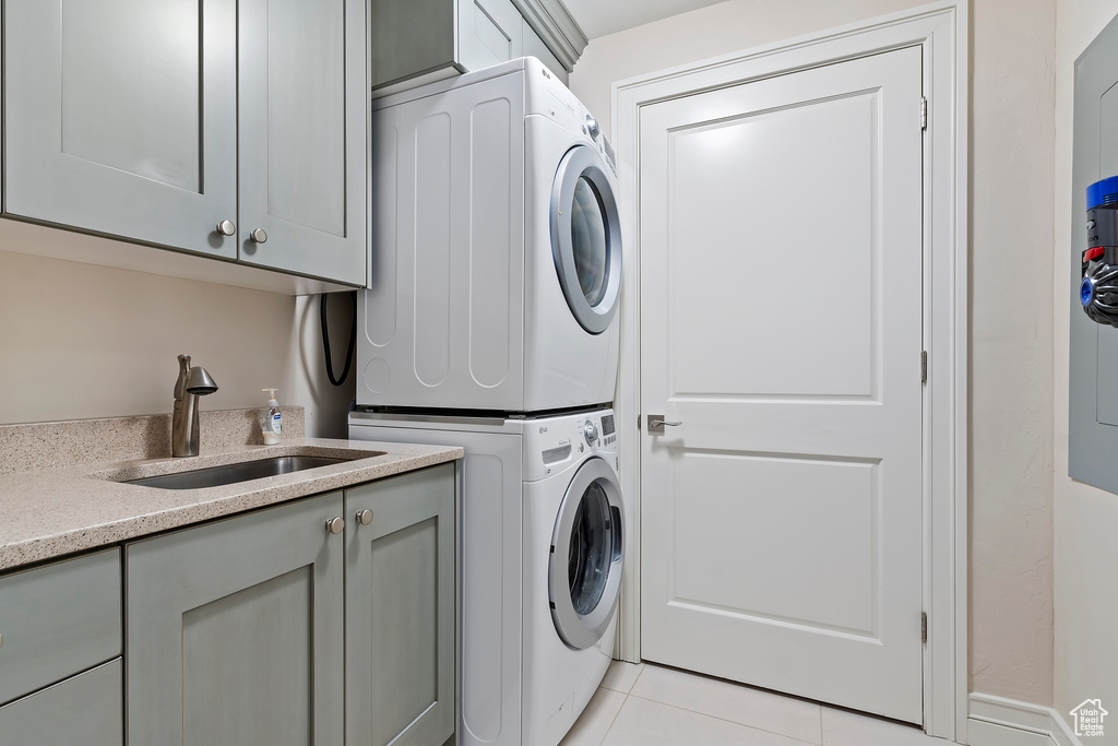 Laundry room featuring sink, light tile flooring, stacked washing maching and dryer, and cabinets