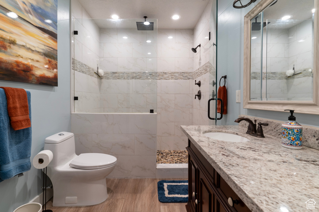 Bathroom with toilet, tile walls, a tile shower, vanity with extensive cabinet space, and wood-type flooring