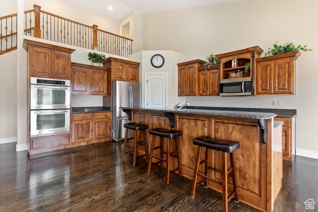 Kitchen featuring stainless steel appliances, a breakfast bar, dark stone countertops, a towering ceiling, and dark hardwood / wood-style floors