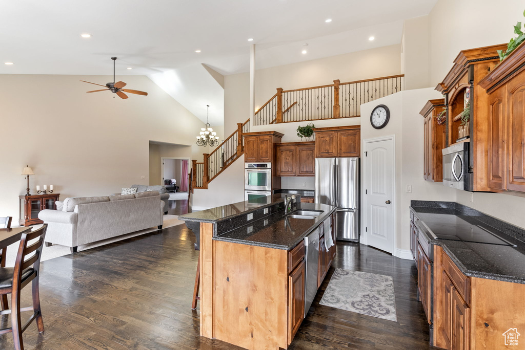 Kitchen with a center island, dark wood-type flooring, ceiling fan with notable chandelier, high vaulted ceiling, and appliances with stainless steel finishes