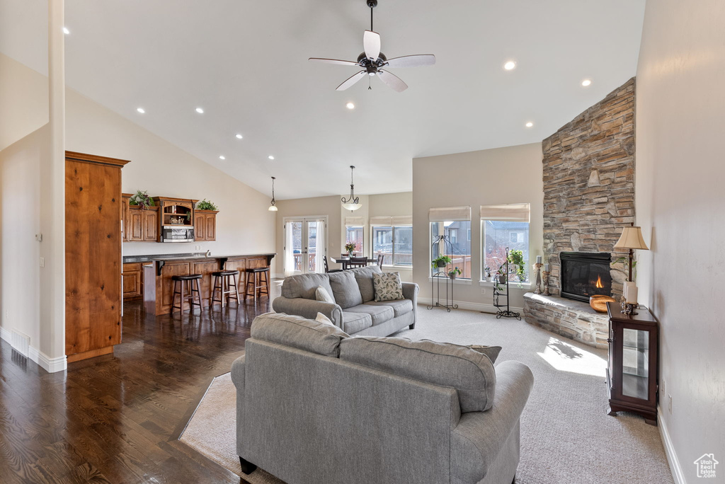 Living room featuring a stone fireplace, dark hardwood / wood-style flooring, ceiling fan, and high vaulted ceiling