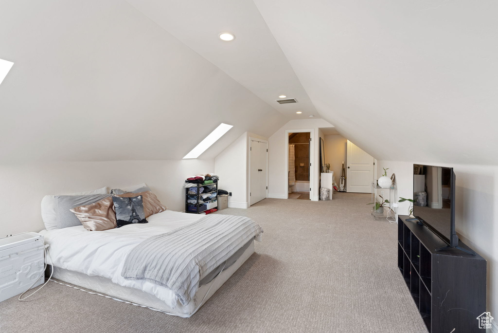 Bedroom featuring light carpet, ensuite bath, and lofted ceiling with skylight