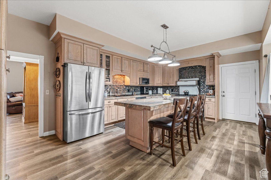 Kitchen featuring a kitchen island, backsplash, hardwood / wood-style flooring, decorative light fixtures, and appliances with stainless steel finishes