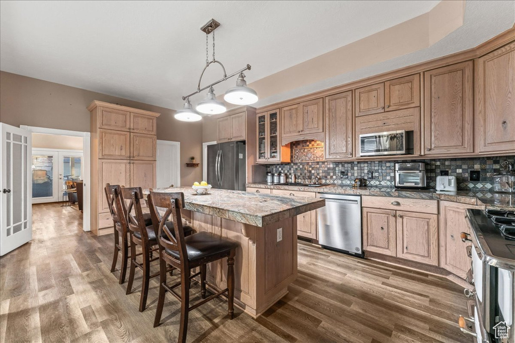 Kitchen with french doors, appliances with stainless steel finishes, decorative light fixtures, wood-type flooring, and a center island