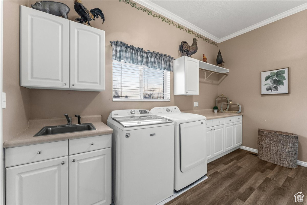 Clothes washing area with ornamental molding, washer and clothes dryer, sink, dark hardwood / wood-style floors, and cabinets