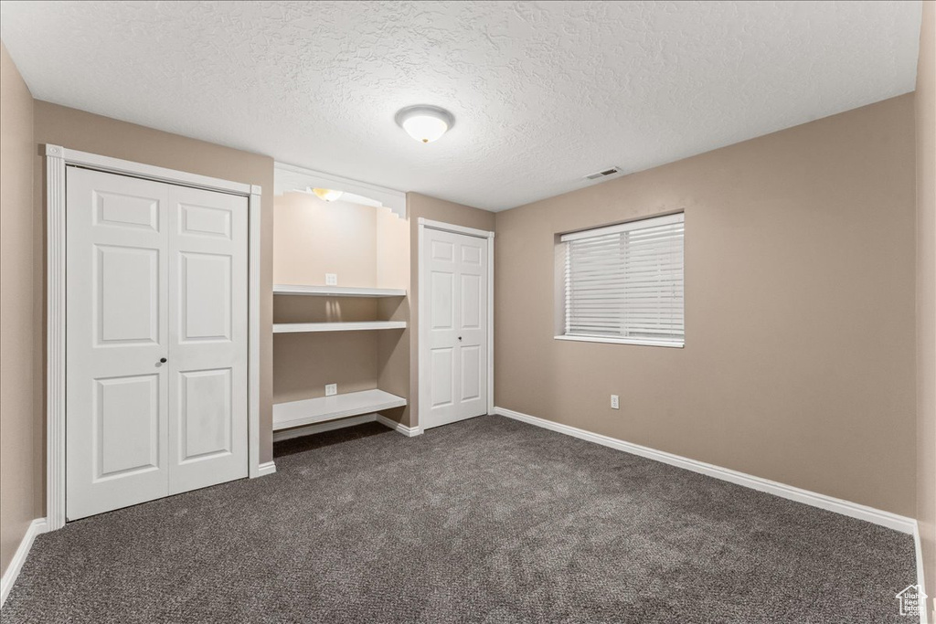 Unfurnished bedroom with a textured ceiling and dark carpet