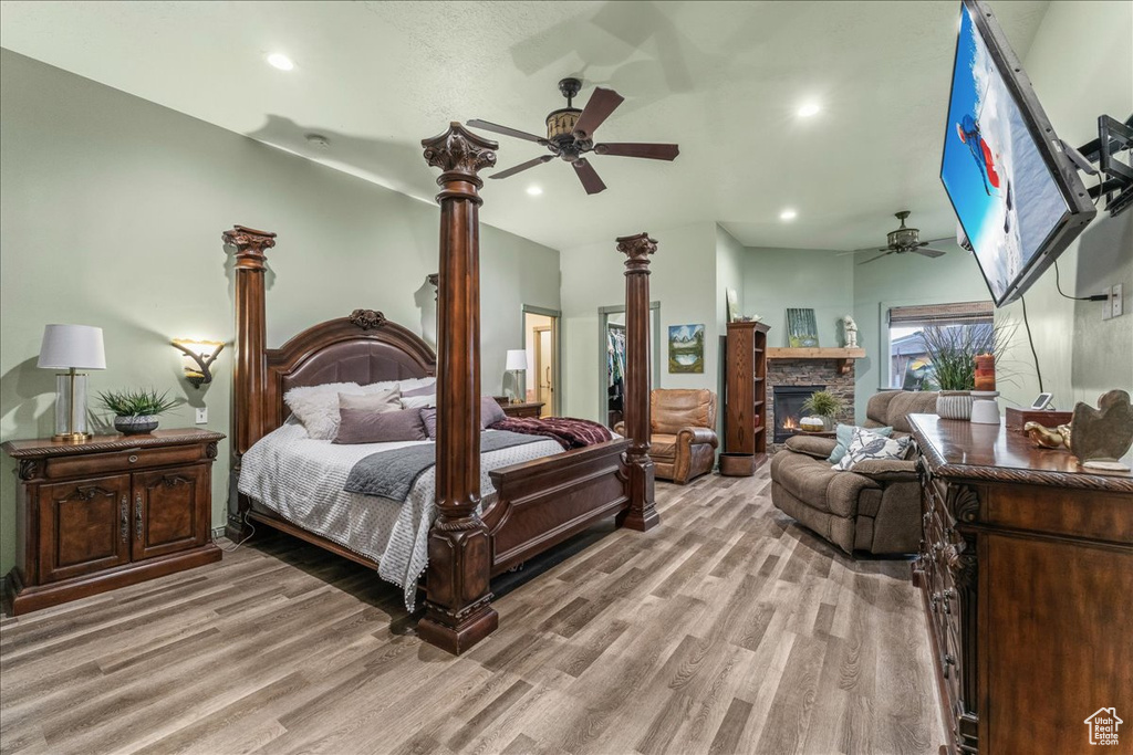Bedroom with ceiling fan, a stone fireplace, and light wood-type flooring