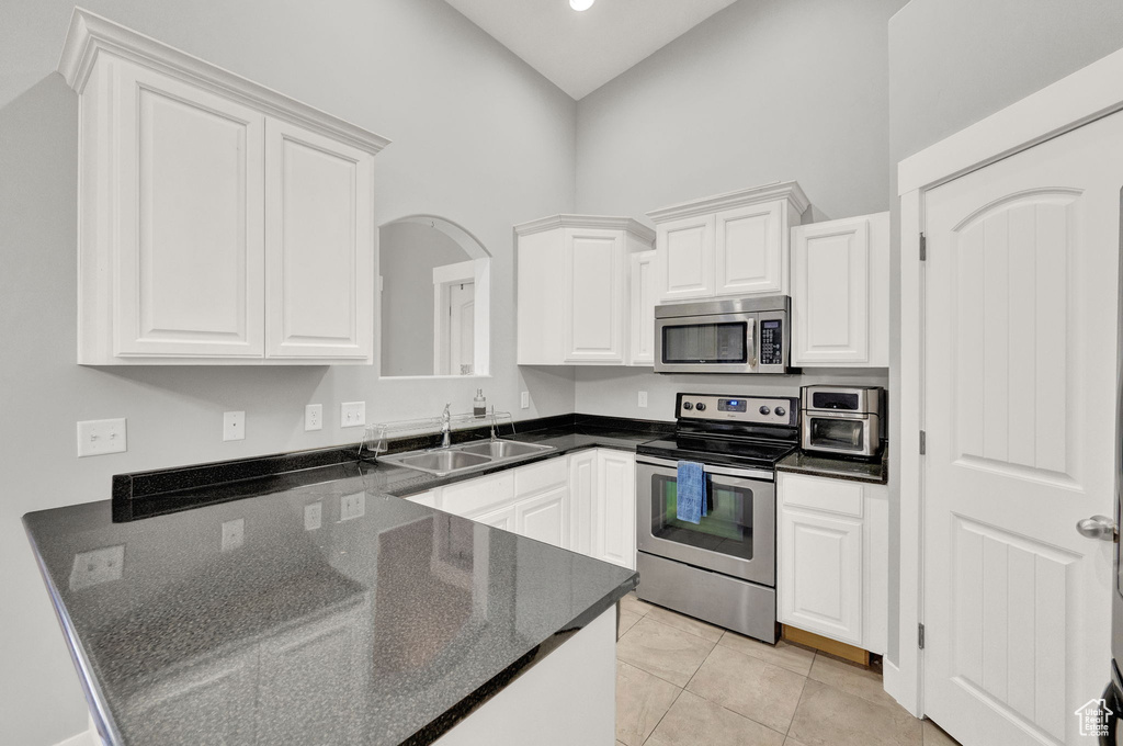 Kitchen featuring sink, light tile floors, stainless steel appliances, and white cabinets