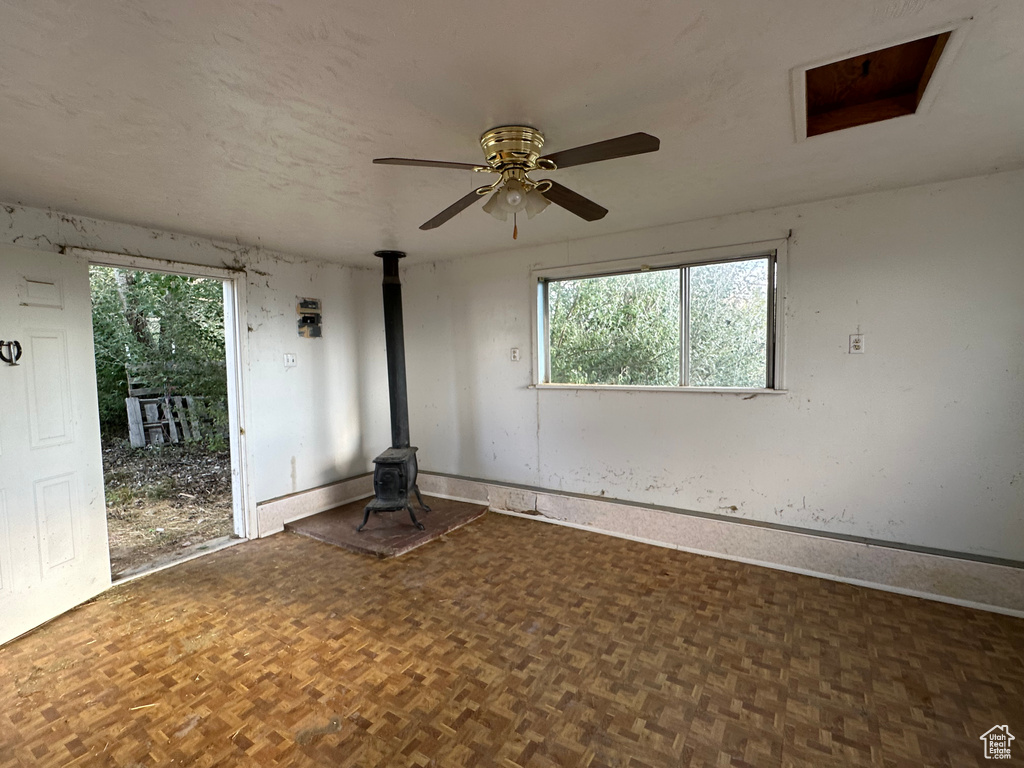 Unfurnished room featuring plenty of natural light, ceiling fan, dark parquet flooring, and a wood stove