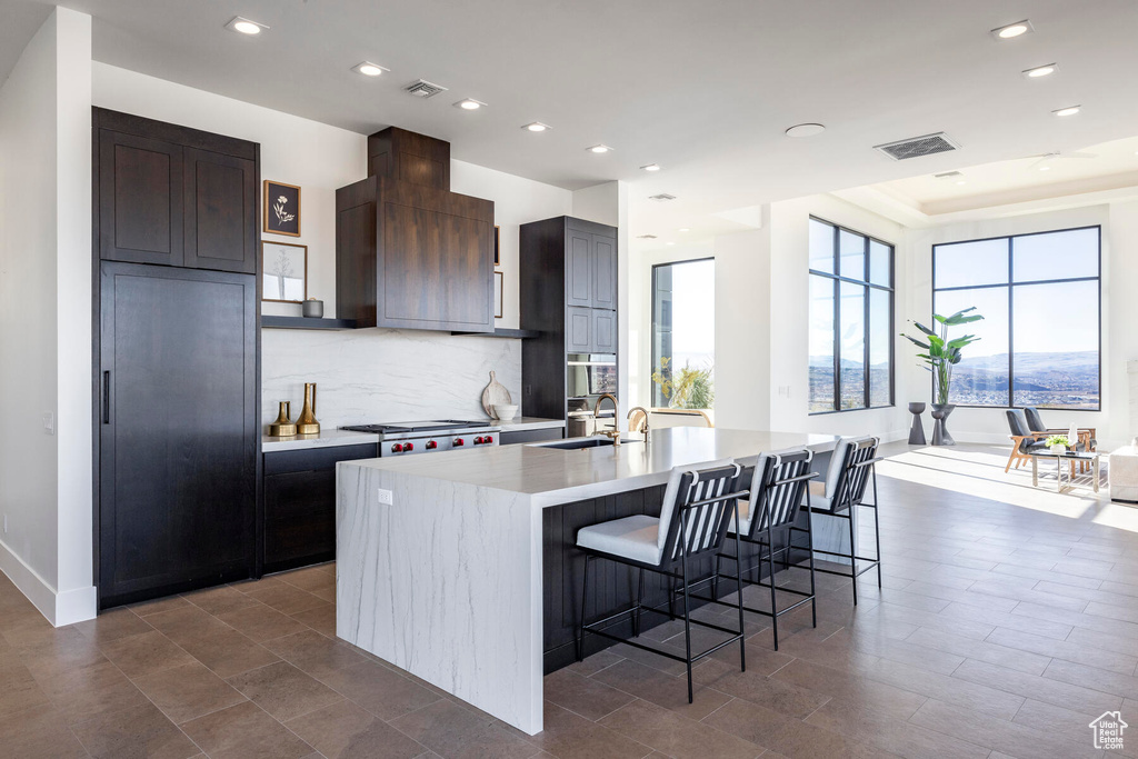 Kitchen featuring dark brown cabinetry, sink, stove, a center island with sink, and a breakfast bar