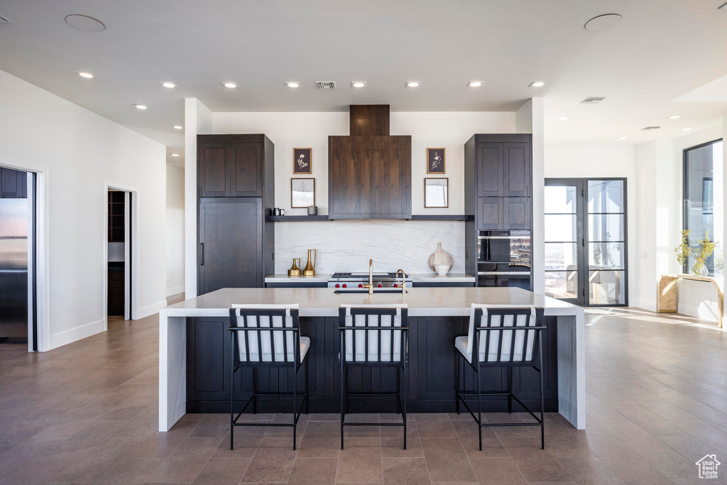 Kitchen featuring black double oven, a breakfast bar, a center island with sink, and backsplash