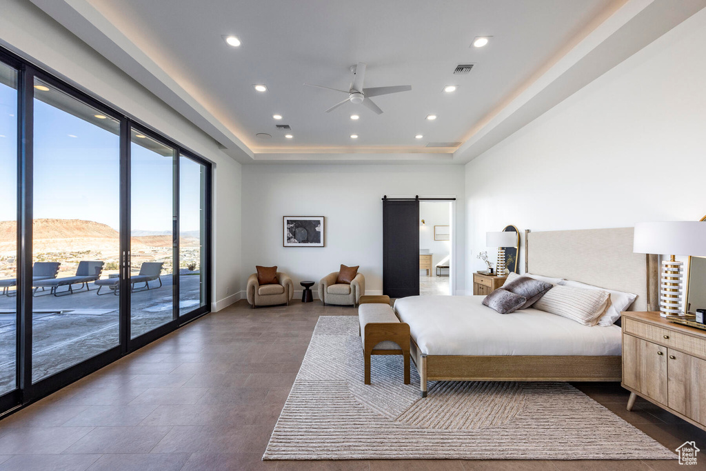 Bedroom featuring a raised ceiling, a barn door, ceiling fan, and access to exterior