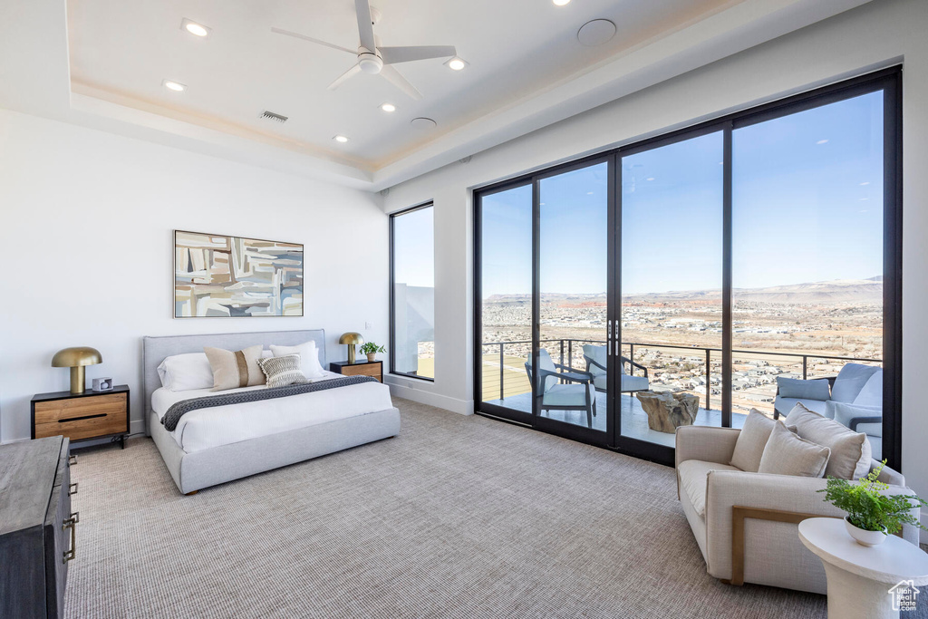 Carpeted bedroom with a tray ceiling, access to exterior, and ceiling fan