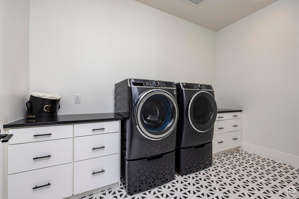 Laundry room featuring separate washer and dryer, cabinets, and light tile patterned floors